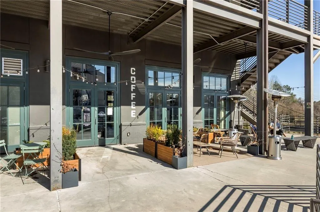 Exposed structural steel beams, concrete patio, full-light entry doors, string lighting, and built-in planters