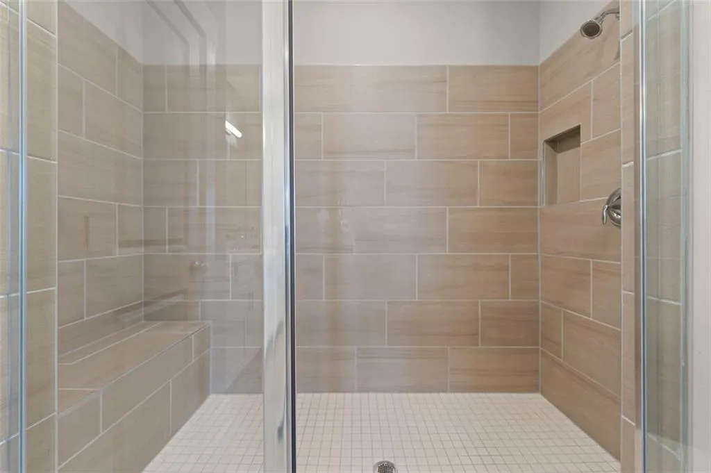 Glass-enclosed shower with large format wall tiles, built-in bench, recessed shelf, and chrome fixtures