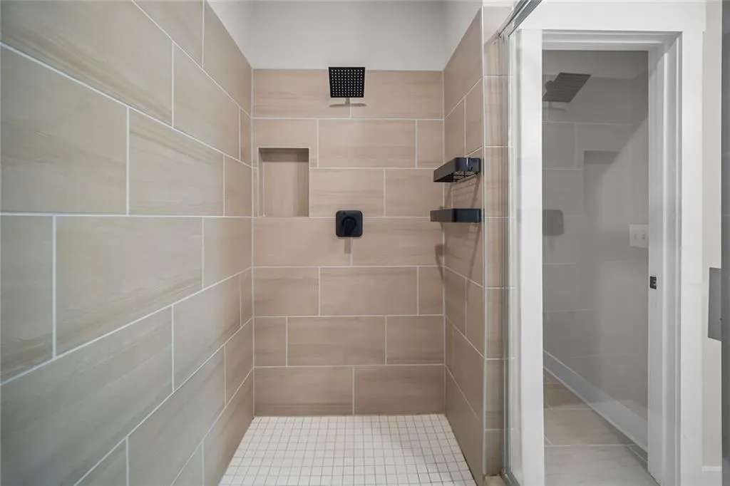 Shower featuring textured tile walls, a built-in niche, matte black fixtures, and a glass-enclosed entry