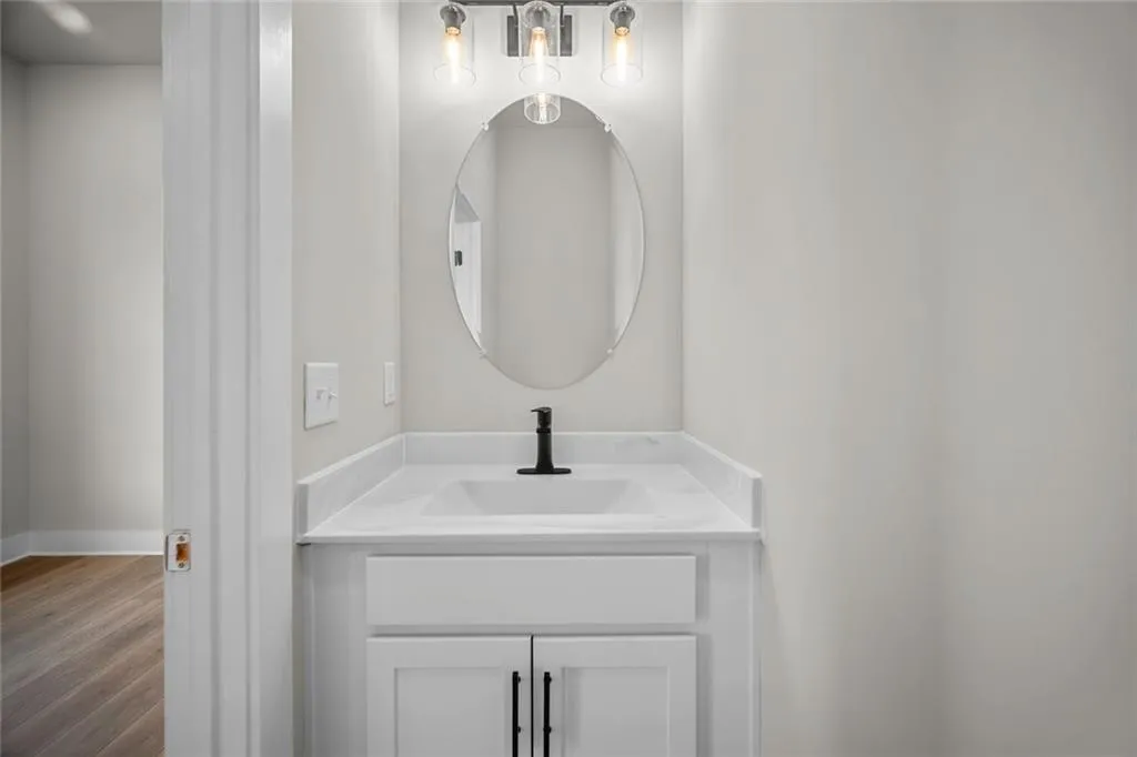 White vanity with shaker-style cabinetry, a white countertop, an oval mirror, and a matte black faucet