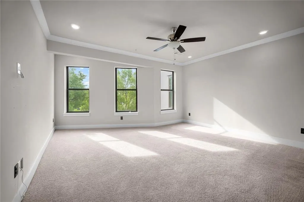 Spacious room with plush carpeting, three large windows, recessed lighting, and a ceiling fan