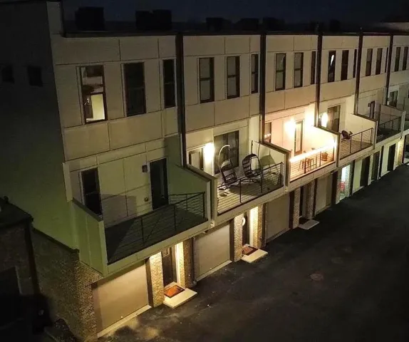 Multi-level townhomes/condos exterior featuring private balconies with metal railings, individual garage doors, brick accents, and a modern facade
