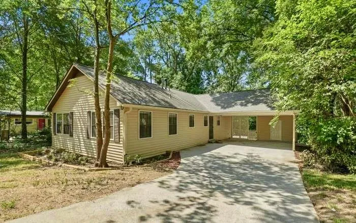 Siding exterior with dark shutters, gabled roofline, and a paved driveway leading to a covered carport
