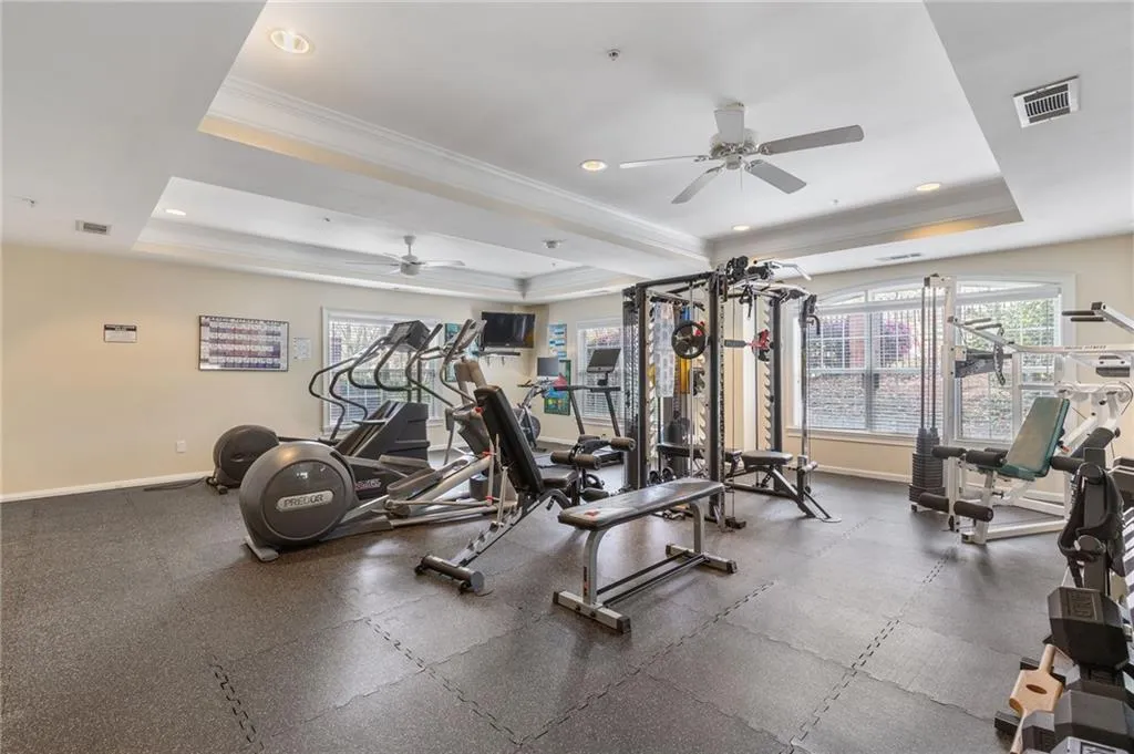 Gym featuring crown molding, a raised ceiling, recessed lighting, and a ceiling fan