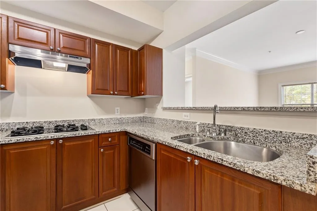 Kitchen featuring stainless steel appliances, light stone counters, ornamental molding, wood finish cabinetry, and light tile patterned flooring