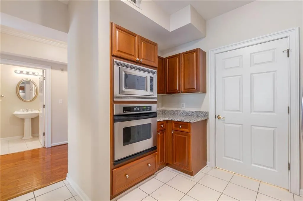 Kitchen featuring light tile patterned floors, stainless steel appliances, wood finish cabinetry, and light stone countertops