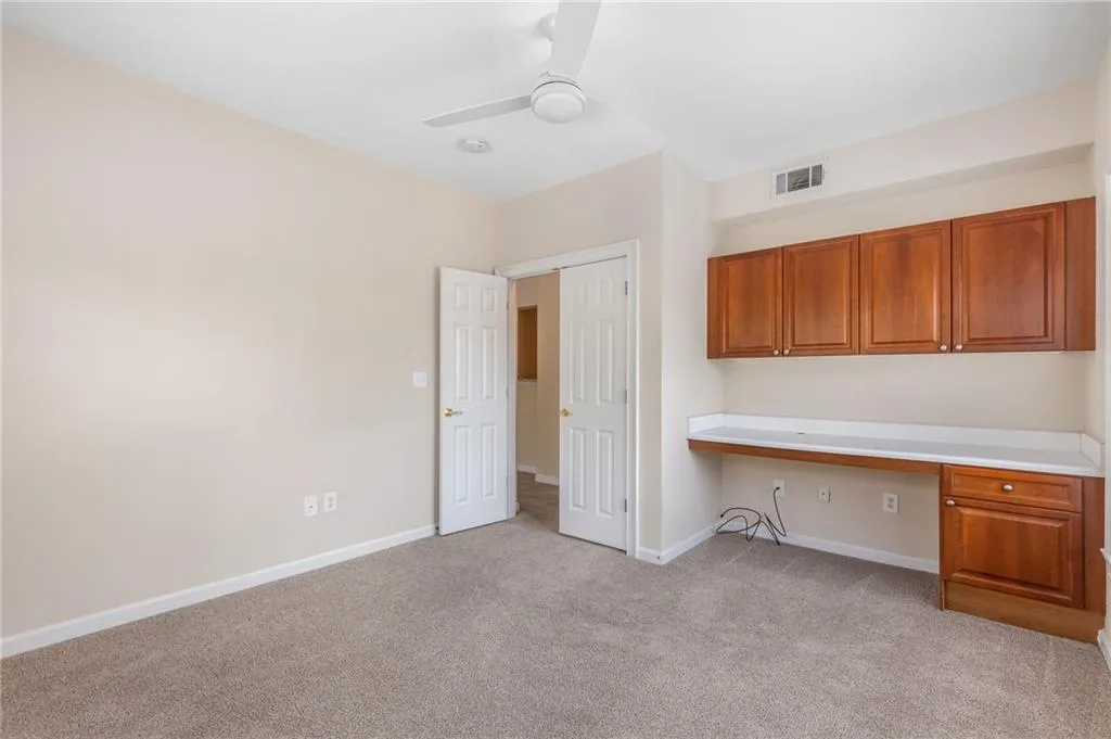 Unfurnished office featuring built in desk, light colored carpet, and ceiling fan