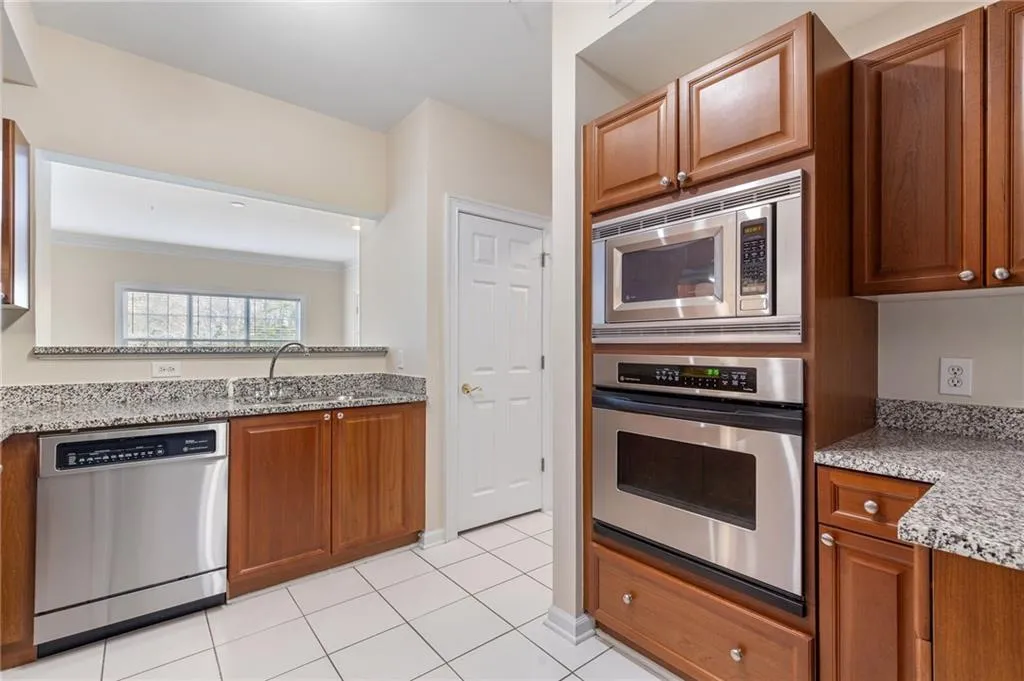 Kitchen featuring light stone countertops, stainless steel appliances, wood finish cabinetry, light tile patterned flooring, and ornamental molding