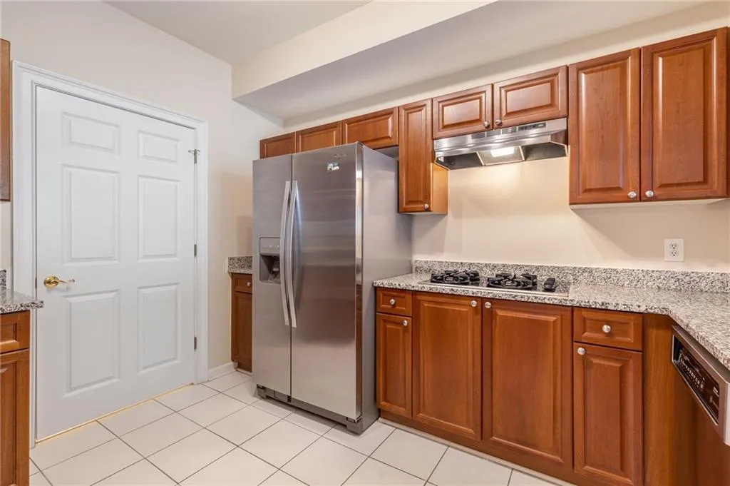Kitchen featuring wood finish cabinets, stainless steel appliances, light stone countertops, and light tile patterned flooring