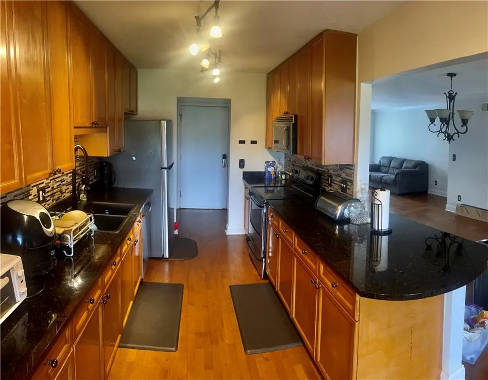 Kitchen with appliances with stainless steel finishes, a sink, brown cabinetry, backsplash, and light wood finished floors