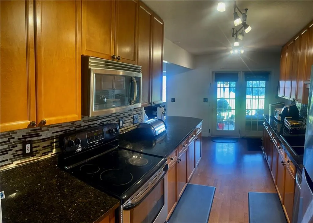 Kitchen featuring appliances with stainless steel finishes, backsplash, dark stone countertops, wood finished floors, and brown cabinets