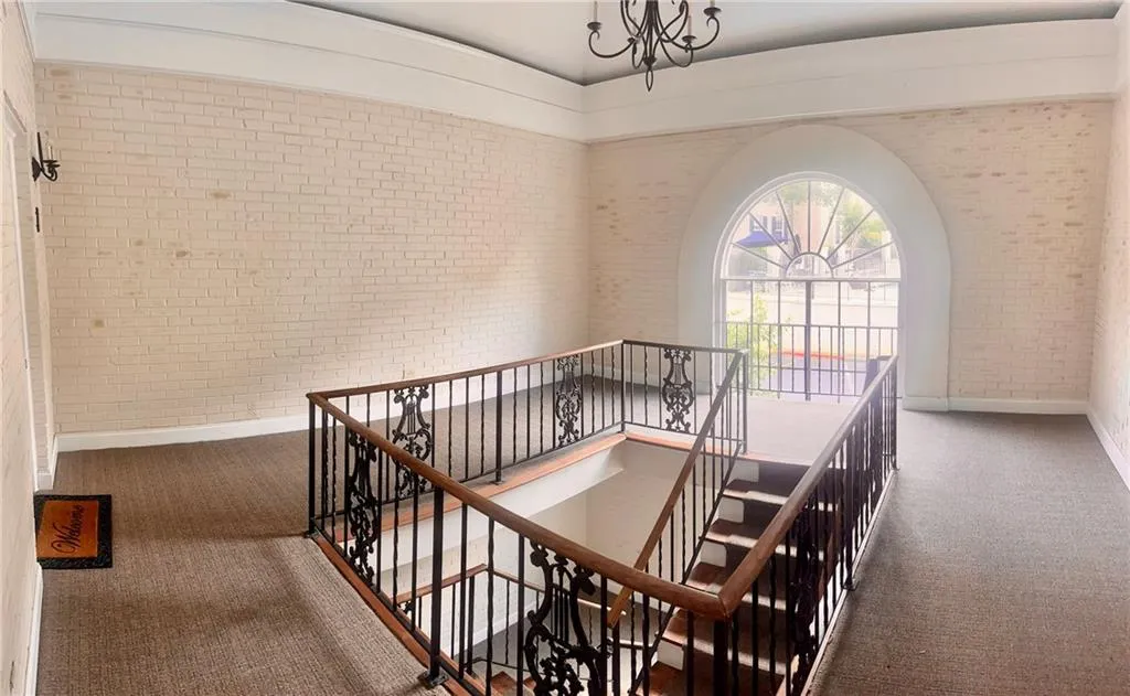 Common area entrance Stairs with brick wall, new carpet floors, baseboards, and a chandelier