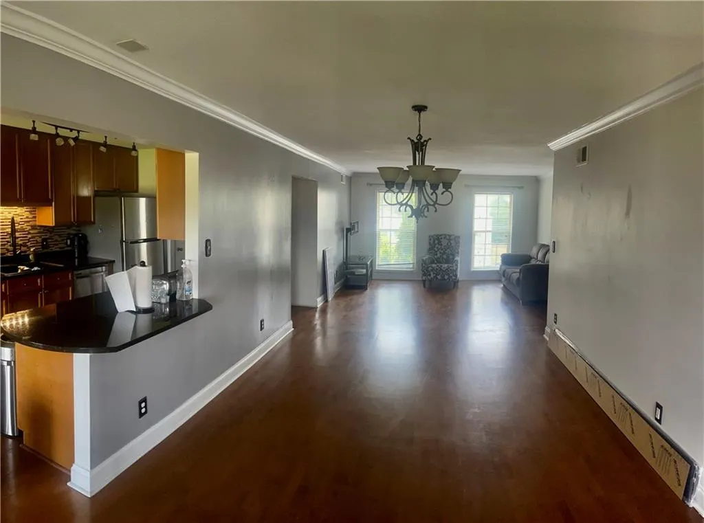 Unfurnished dining area featuring dark wood-style floors, a chandelier, baseboards, ornamental molding, and a sink