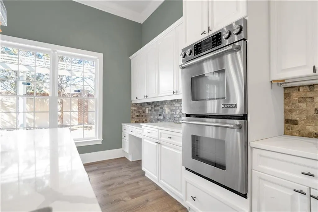 Kitchen with tasteful backsplash, double oven, light stone counters, and white cabinets