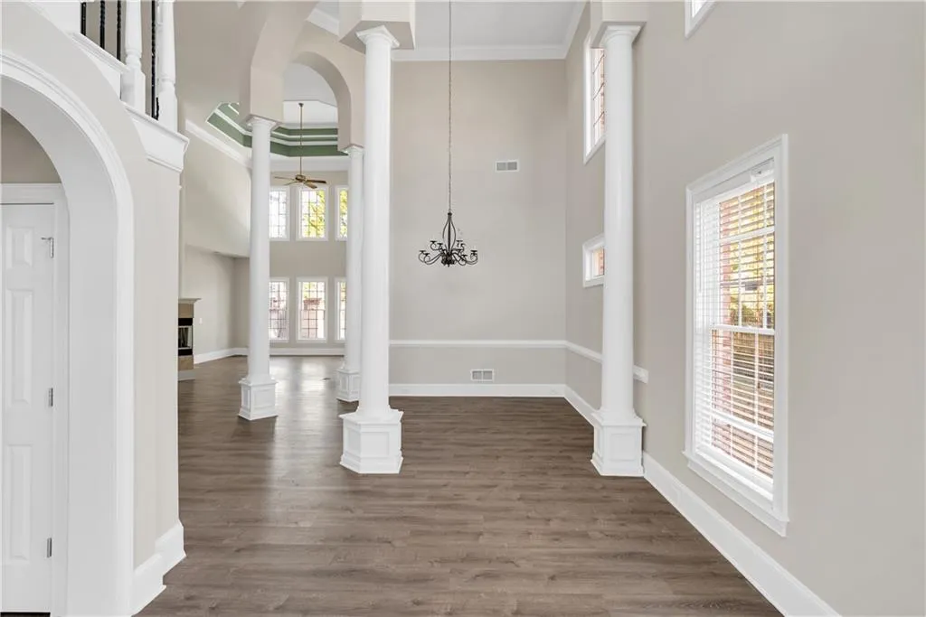 Foyer entrance featuring dark wood-type flooring, a high ceiling, visible vents, ornamental molding, and decorative columns