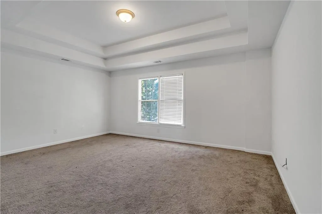 Unfurnished room with carpet, a raised ceiling, visible vents, and baseboards