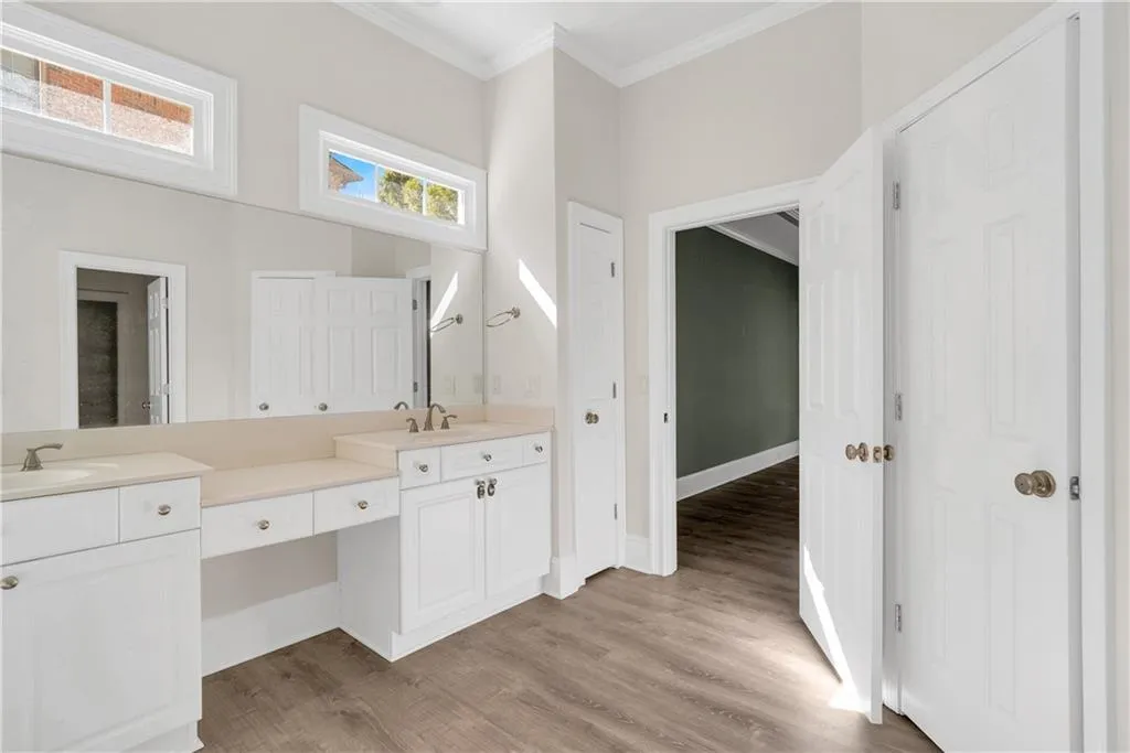 Bathroom featuring a sink, wood finished floors, baseboards, double vanity, and crown molding