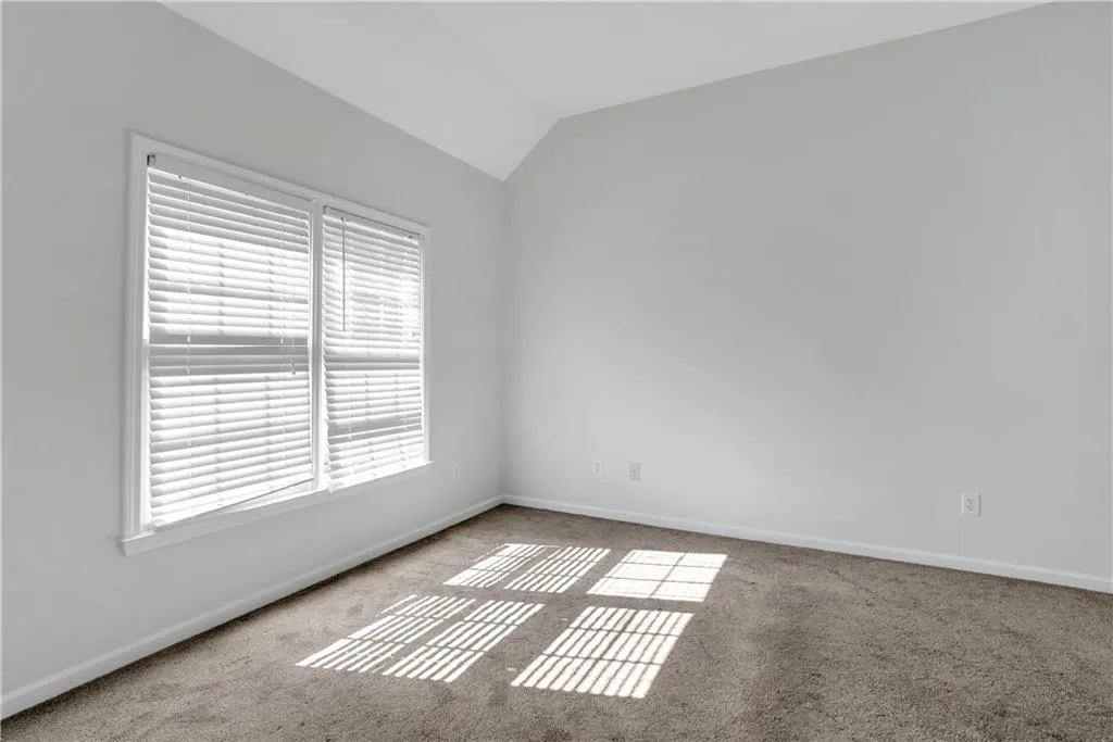 Spare room featuring light carpet, baseboards, and vaulted ceiling