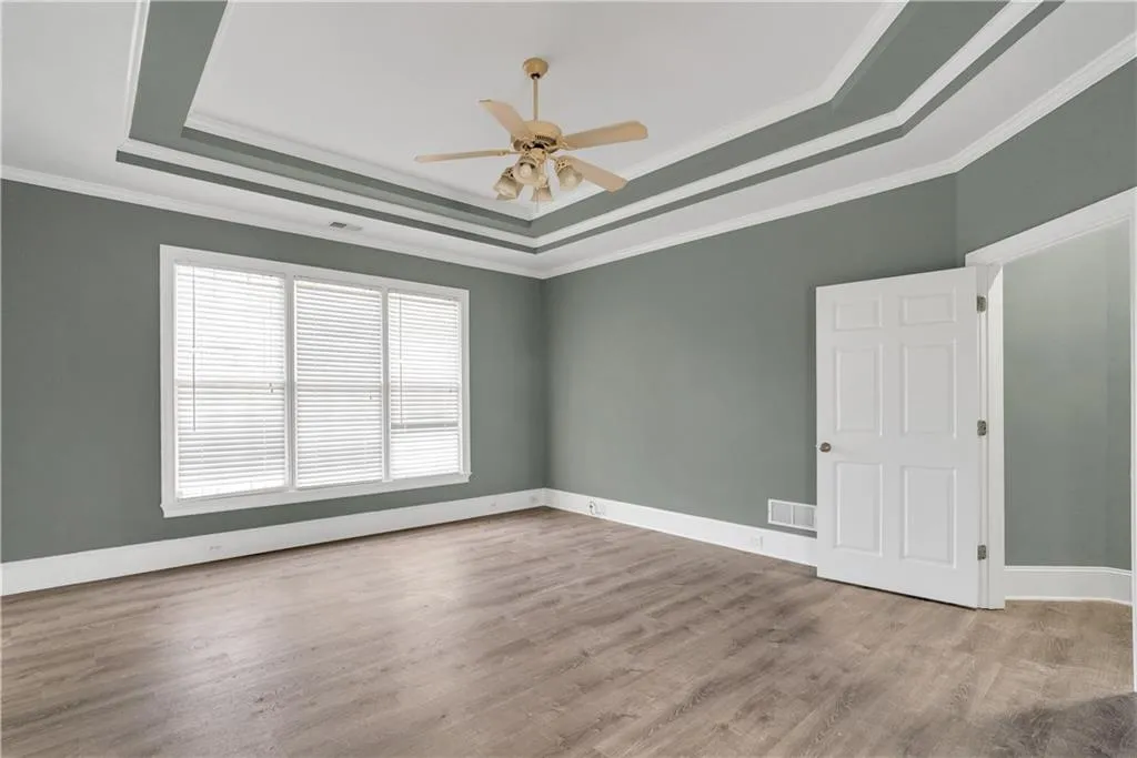 Spare room featuring baseboards, visible vents, a tray ceiling, crown molding, and light wood-type flooring