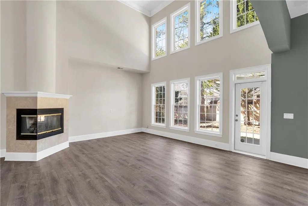 Unfurnished living room featuring baseboards, a tiled fireplace, dark wood-style flooring, a high ceiling, and crown molding