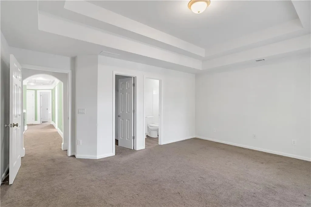 Unfurnished bedroom with baseboards, a tray ceiling, arched walkways, and carpet flooring