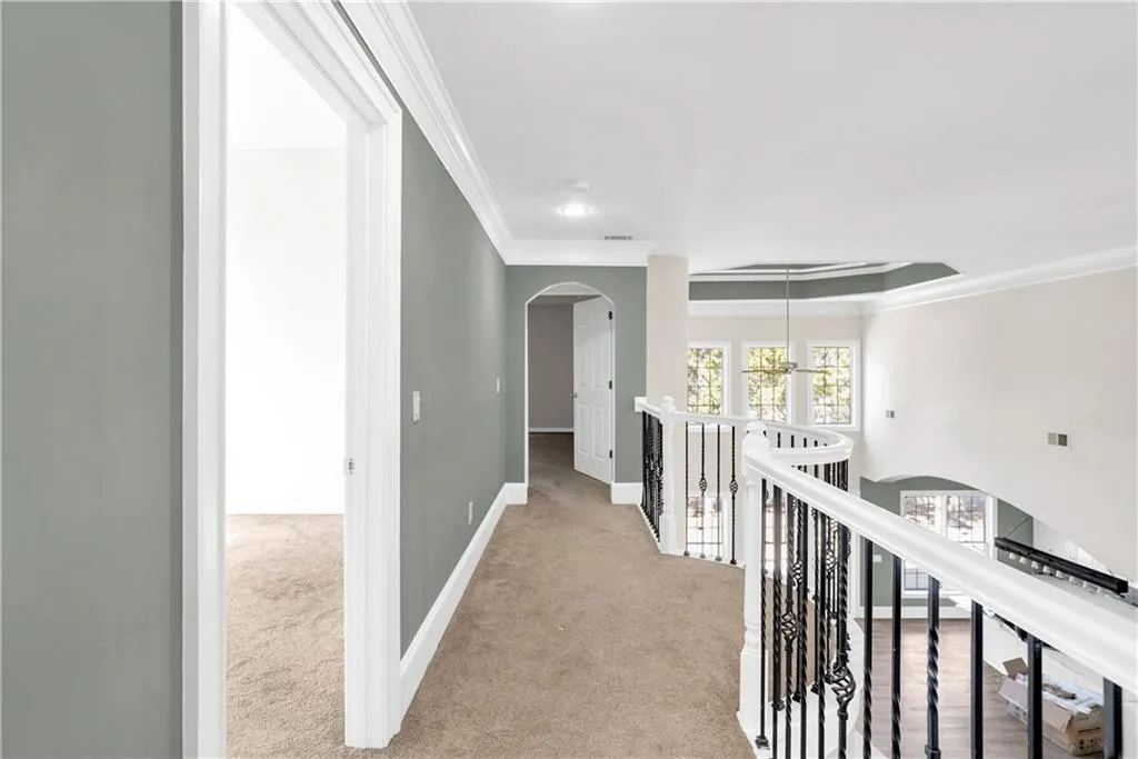 Hall featuring arched walkways, ornamental molding, an upstairs landing, and light colored carpet