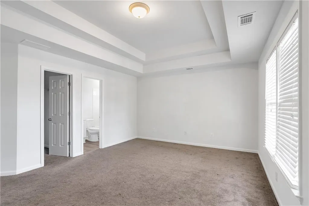 Carpeted spare room with a raised ceiling, visible vents, and baseboards