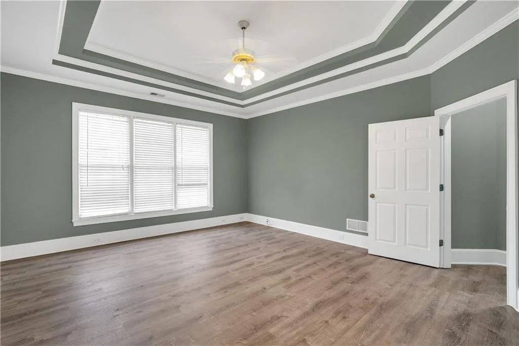Unfurnished room featuring light wood finished floors, visible vents, a raised ceiling, ceiling fan, and ornamental molding