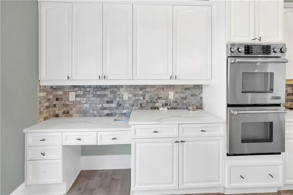Kitchen featuring double oven, white cabinetry, light stone counters, and tasteful backsplash