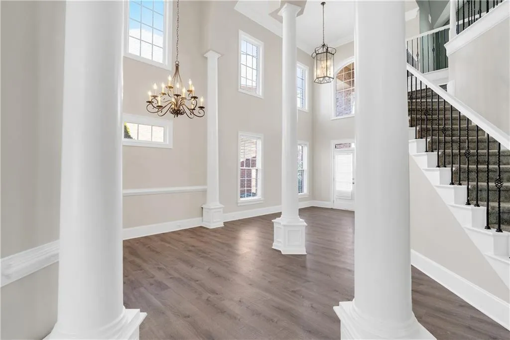 Entrance foyer with decorative columns, ornamental molding, a notable chandelier, and wood finished floors