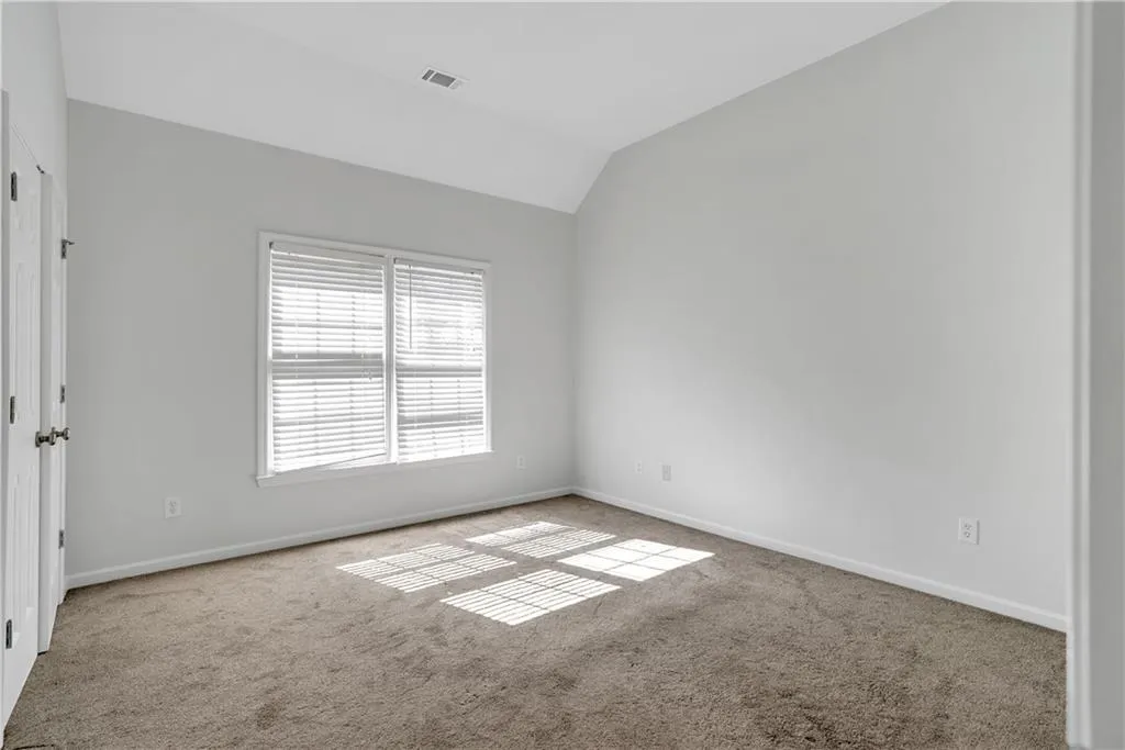 Carpeted spare room featuring baseboards and vaulted ceiling
