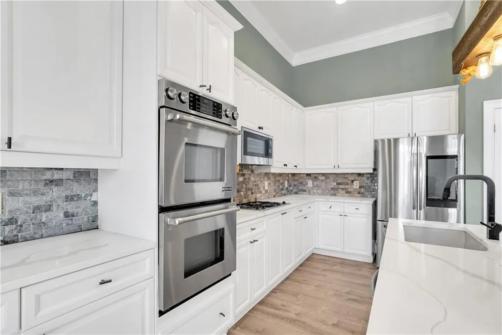 Kitchen with stainless steel appliances, light stone counters, and white cabinetry