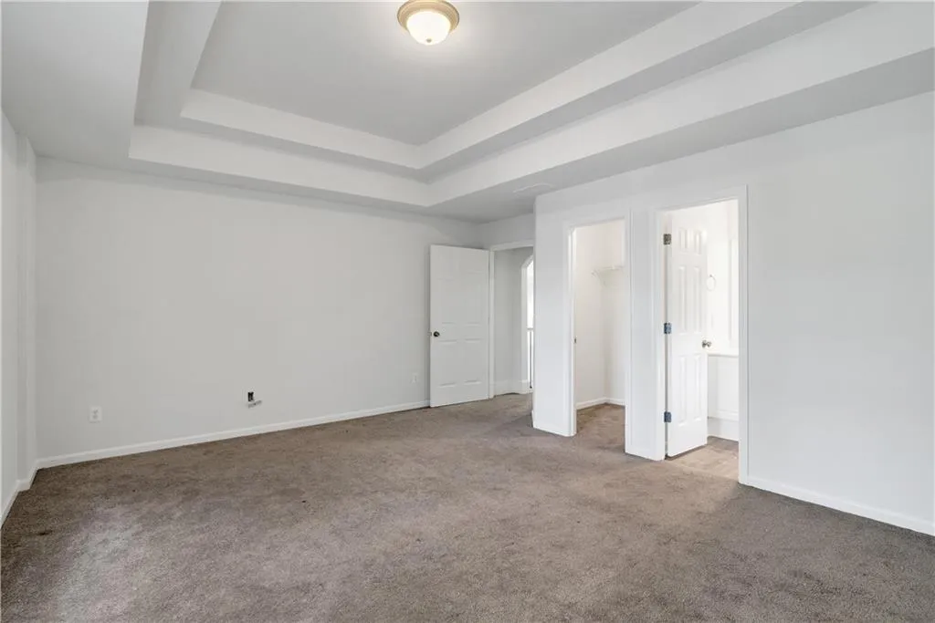 Unfurnished bedroom featuring carpet flooring, baseboards, a spacious closet, a closet, and a raised ceiling