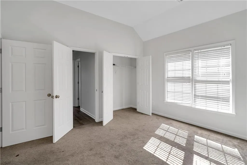Unfurnished bedroom featuring a closet, light colored carpet, vaulted ceiling, and baseboards