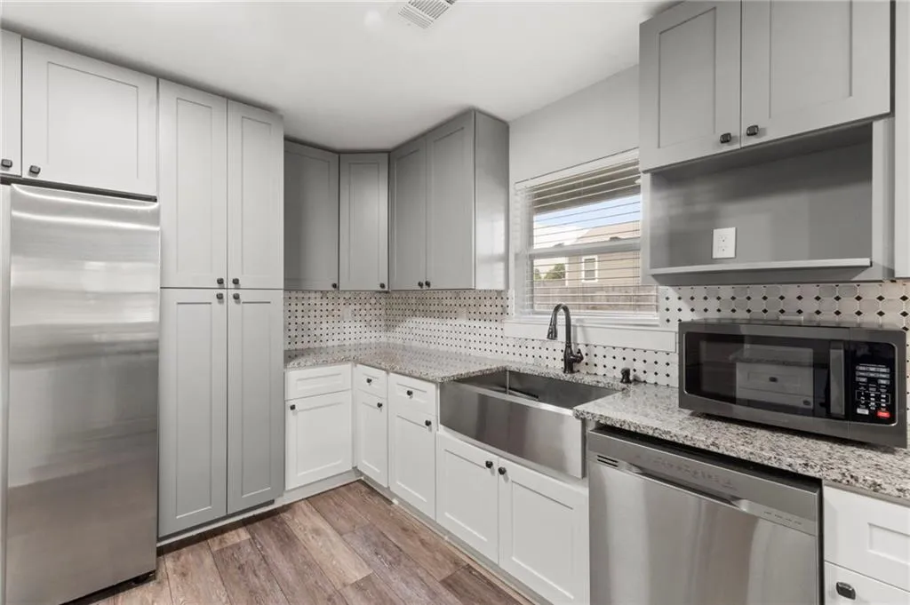 Kitchen featuring appliances with stainless steel finishes, light stone countertops, tasteful backsplash, light wood-style flooring, and gray cabinets