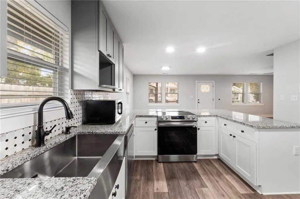 Kitchen featuring a peninsula, stainless steel appliances, dark wood-style flooring, light stone counters, and tasteful backsplash