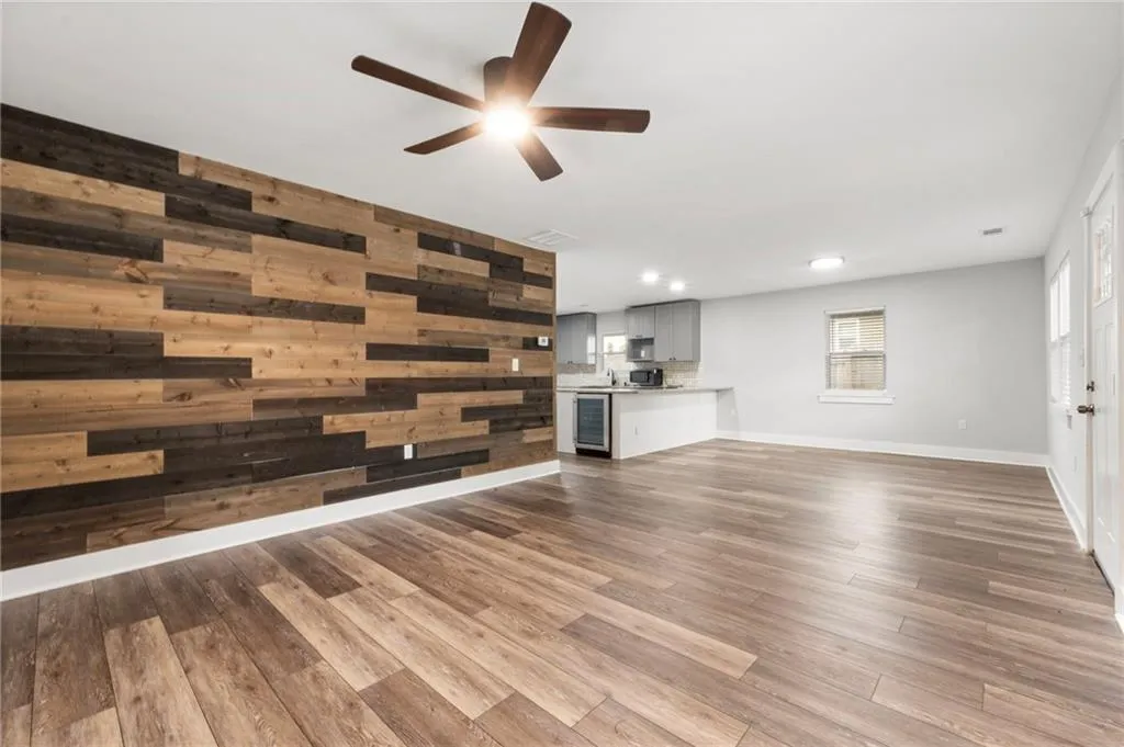 Unfurnished living room with wooden walls, dark wood finished floors, beverage cooler, and ceiling fan