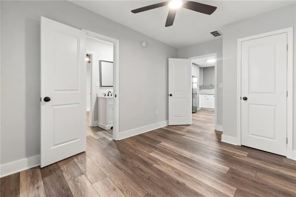 Unfurnished bedroom with connected bathroom, wood finished floors, stainless steel fridge, and ceiling fan