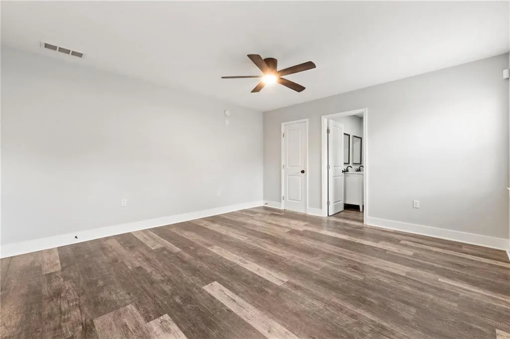 Unfurnished bedroom with wood finished floors, ceiling fan, and ensuite bathroom