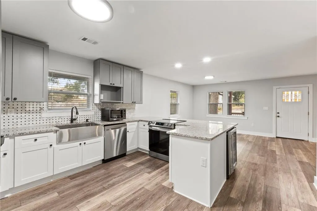 Kitchen featuring tasteful backsplash, light stone countertops, stainless steel appliances, a peninsula, and light wood-style floors