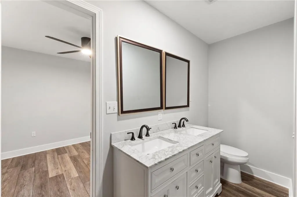 Full bathroom with dark wood-type flooring, double vanity, and a ceiling fan