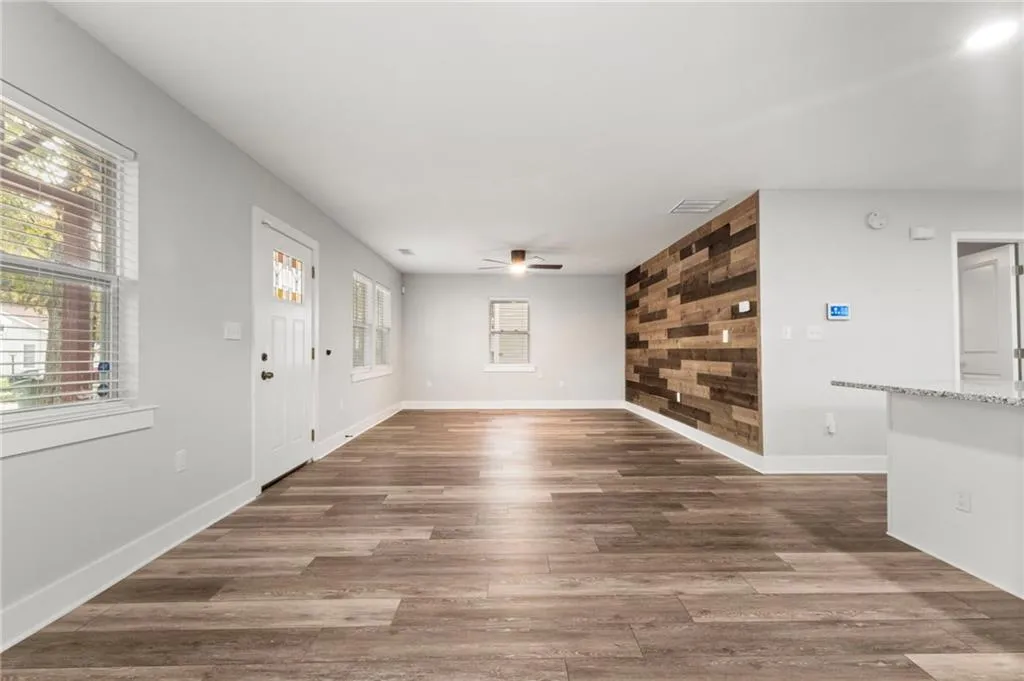 Unfurnished living room featuring dark wood-style floors, wood walls, and a ceiling fan
