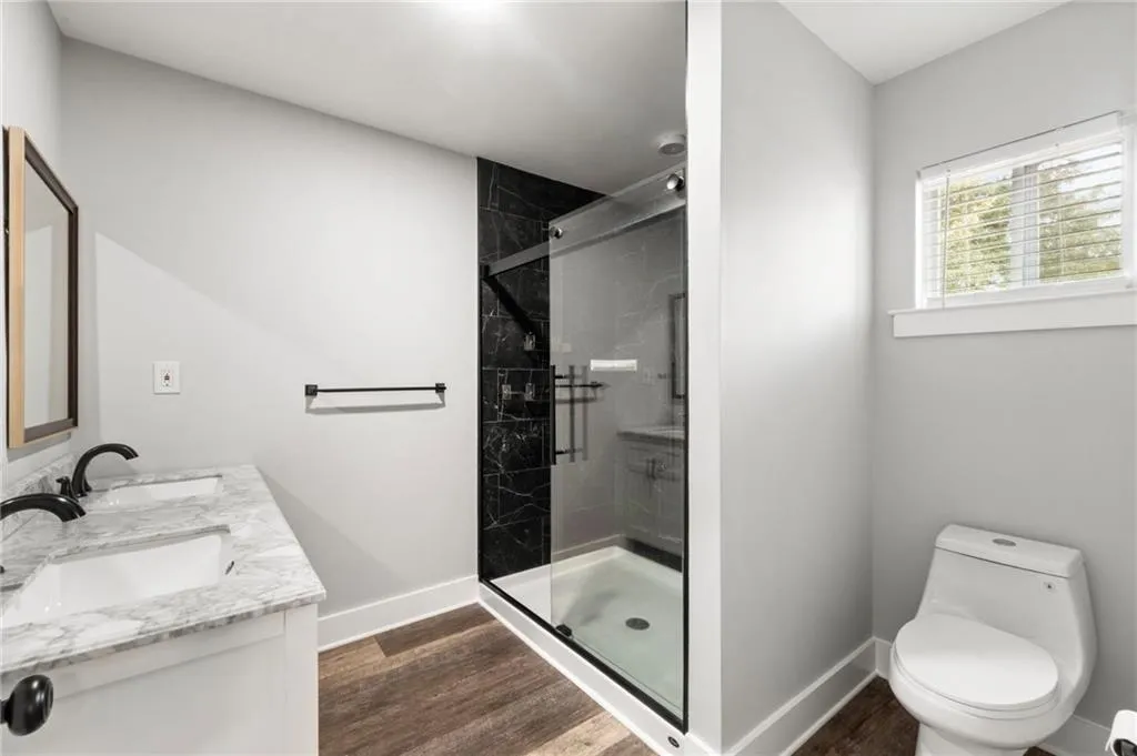 Bathroom with a shower stall, double vanity, and dark wood-style flooring