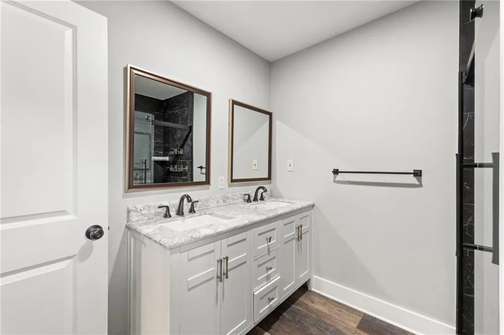 Full bathroom featuring a marble finish shower, double vanity, and dark wood-style flooring