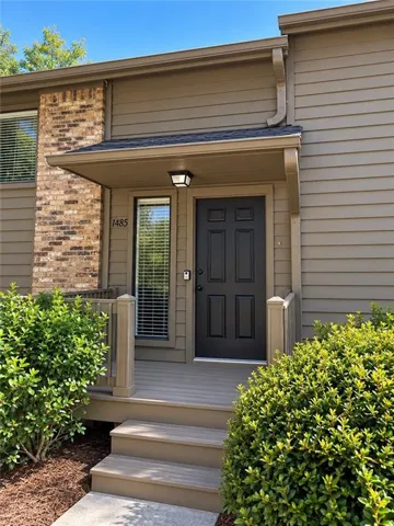 Front entry with a dark paneled door, composite decking, and brick veneer accents