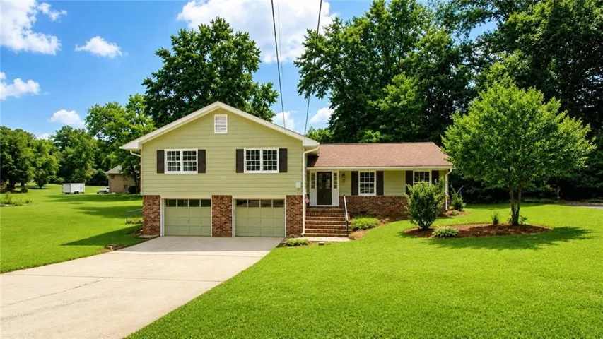 Split-level dwelling featuring a two-car garage with brick accents, expansive driveway, and a front entry with brick steps