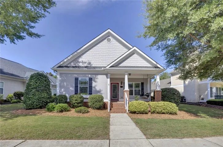 Gabled roofline with shingle siding accents, covered front porch, brick front steps, established landscaping, and a concrete walkway
