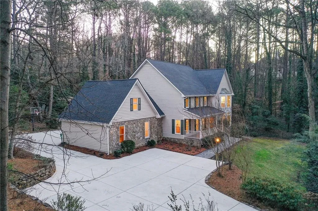 View of front facade with stone siding, covered porch, roof with shingles, concrete driveway, and a front yard