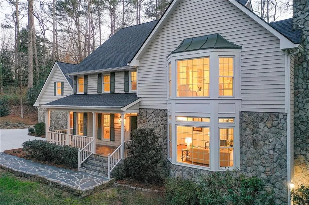 Rear view of house with stone siding, a porch, and roof with shingles