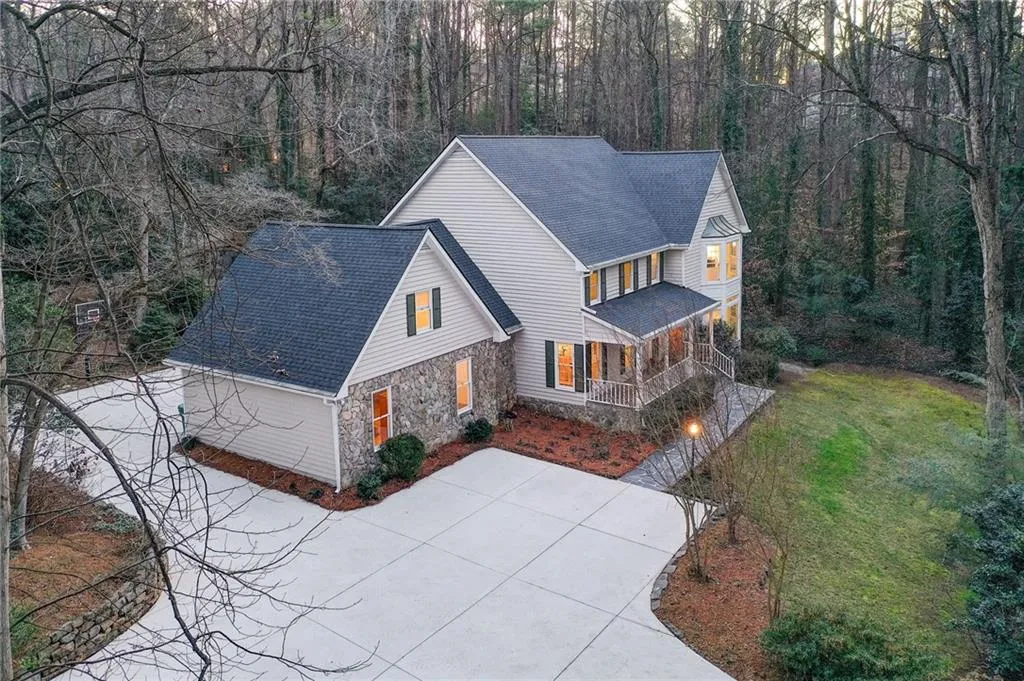View of front of property with a porch, a shingled roof, stone siding, a front lawn, and concrete driveway